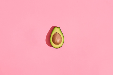 Colorful fruit pattern of fresh cutted avocado halves with pits on coral pink background, top viewの写真素材