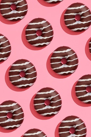 Food design with tasty chocolate glazed donut with white strips on coral pink pastel background top view patternの写真素材