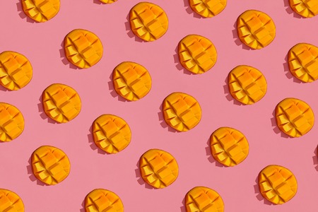 Colorful fruit pattern of fresh juicy cutted mango on coral pink background, top viewの写真素材