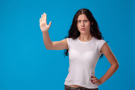 Studio portrait of a young beautiful woman in a white t-shirt against a blue wall background. People sincere emotions.の写真素材