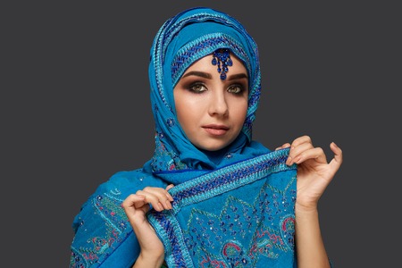 Studio shot of a young beautiful woman wearing the blue hijab decorated with sequins and jewelry....