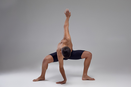 Photo of a handsome man ballet dancer, dressed in a black shorts, making a dance element against a gray background in studio.の写真素材