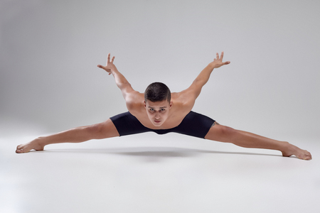 Photo of a handsome man ballet dancer, dressed in a black shorts, making a dance element against a gray background in studio.の写真素材