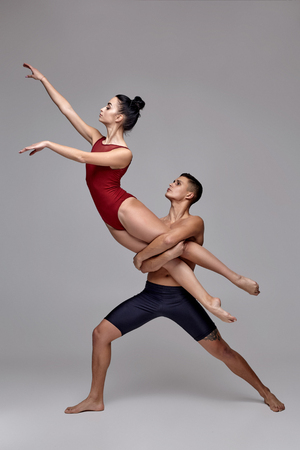 The couple of an athletic modern ballet dancers are posing against a gray studio background.の写真素材