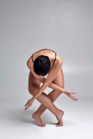 Studio photo of a beautiful woman ballerina dressed in black two-piece swimsuit doing a dance element on a gray background.の写真素材