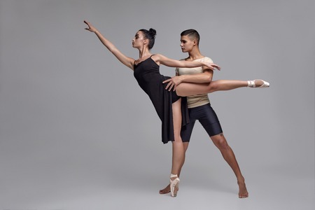 Two athletic modern ballet dancers are posing against a gray studio background.の写真素材