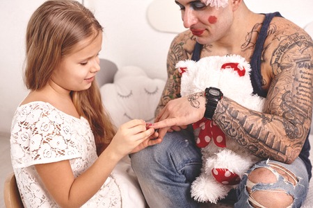 Funny time Tattoed father in a cap and his child are playing at home. Cute girl is doing makeup to her dad in her bedroom. Family holiday togethernessの写真素材