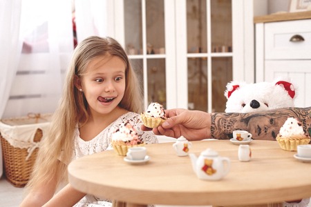 Adorable daughter wearing a white dress whith her loving father. They are drinking tea from a toy dishes in a modern kids room. Happy family.の写真素材