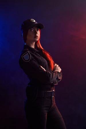 Serious female police officer is posing for the camera against a black background with red and blue backlighting.の写真素材