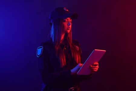 Close-up portrait of a female police officer posing for the camera against a black background with red and blue backlighting.の写真素材
