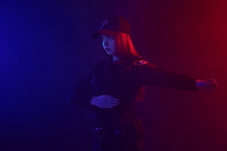 Redheaded female police officer is posing for the camera against a black background with red and...