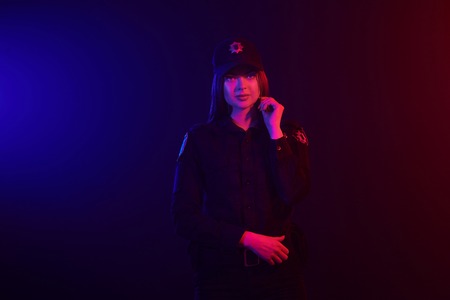 Redheaded female police officer is posing for the camera against a black background with red and...