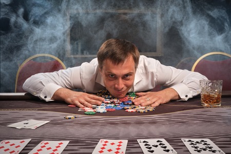 Handsome emotional man is playing poker sitting at the table in casino.の写真素材