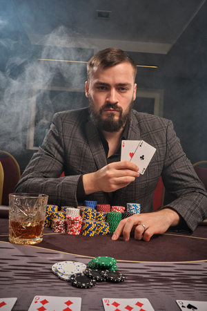 Handsome bearded man is playing poker sitting at the table in casino.