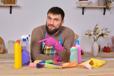 Young handsome bearded man in the kitchen, shows all his cleaning staff - detergents, brushes, sprays. He think he is ready for real cleaningの写真素材