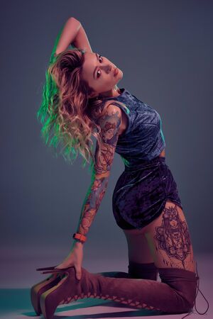 Attractive young blonde girl in blue velour booty shorts and maroon suede high boots posing on camera in studioの写真素材