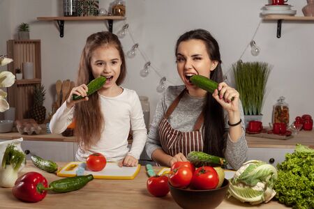 Mother and her daughter are making a vegetable salad and having fun at the kitchen.の写真素材