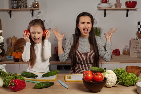 Mother and her daughter are making a vegetable salad and having fun at the kitchen.の写真素材