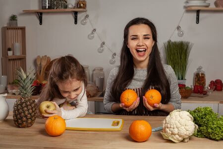Mother and her daughter are doing a fruit cutting and having fun at the kitchen.の写真素材
