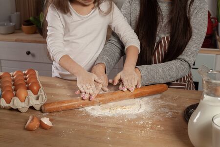 Mother and her daughter are baking a bread and having fun at the kitchen.
