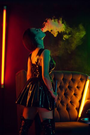 Sexy brunette model is smoking a hookah exhaling a smoke at a luxury night club.の写真素材