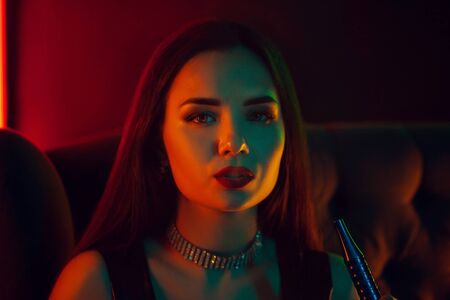 Sexy brunette model is smoking a hookah exhaling a smoke at a luxury night club.