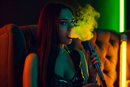 Sexy brunette model is smoking a hookah exhaling a smoke at a luxury night club.の写真素材