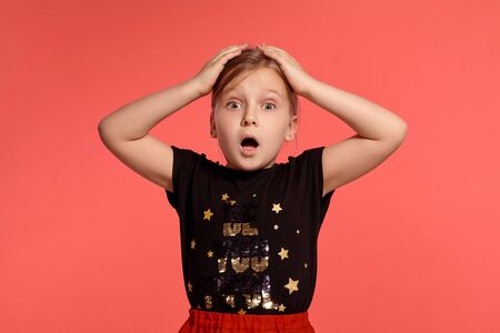 Close-up shot of a charming blonde little lady in a combined dress posing against a pink background.