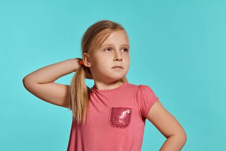 Close-up shot of beautiful blonde little girl in a pink dress posing against a blue background.
