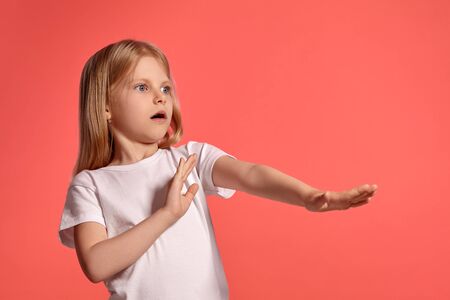Close-up studio shot of a nice blonde little girl in a white t-shirt posing against a pink background.の写真素材