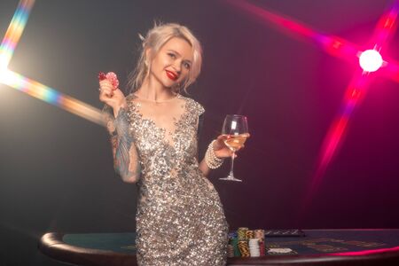 Blonde woman with a beautiful hairstyle and perfect make-up is posing with red gambling chips in her hands. Casino, poker.の写真素材