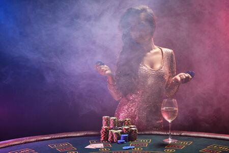 Brunette girl with a perfect hairstyle and bright make-up is posing with gambling chips in her hands. Casino, poker.の写真素材