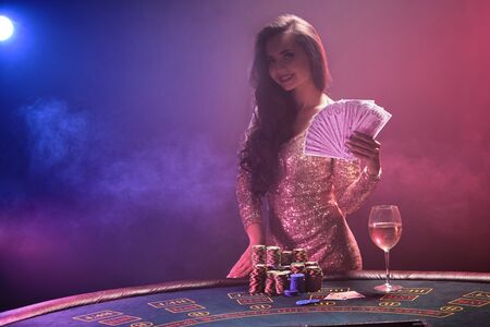 Brunette girl with a perfect hairstyle and bright make-up is posing with fan of hundred dollar bills...