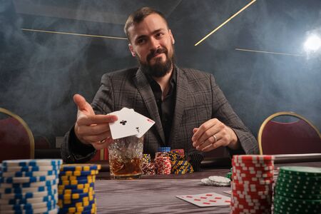 Handsome bearded man is playing poker sitting at the table in casino.の写真素材
