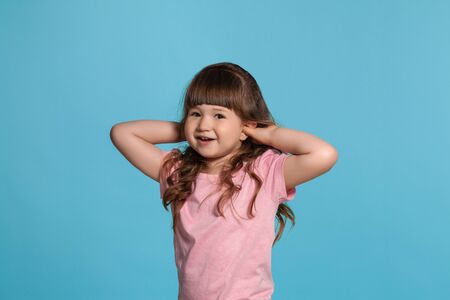 Beautiful little girl wearing in a pink t-shirt is posing against a blue studio background.