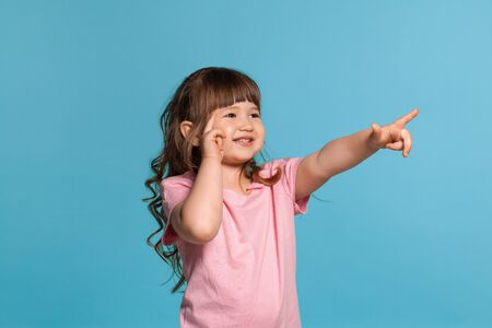 Beautiful little girl wearing in a pink t-shirt is posing against a blue studio background.の写真素材