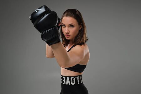 Athletic woman in boxing gloves is practicing karate in studio.