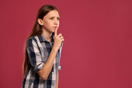 Beautiful teenage girl in a casual checkered shirt is posing against a pink studio background.の写真素材