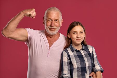 Beautiful teenage girl with her grandfather posing against a pink studio background.