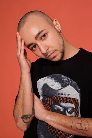 Studio shot of a young tattooed bald man posing against a pink