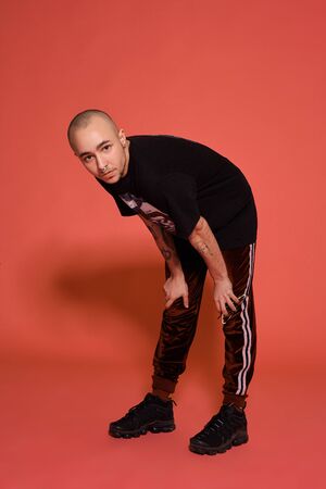Studio shot of a young tattooed bald man posing against a pinkの写真素材
