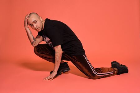 Studio shot of a young tattoed bald man posing against a pink background. 90s style.