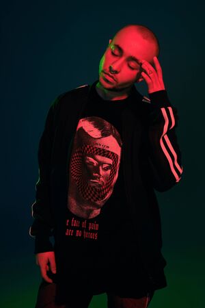 Studio shot of a young tattoed bald man posing against a colorful background. 90s style.