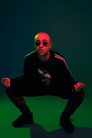 Studio shot of a young tattoed bald man posing against a colorful background. 90s style.