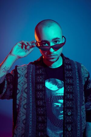 Studio shot of a young tattoed bald man posing against a blue background. 90s style.の写真素材