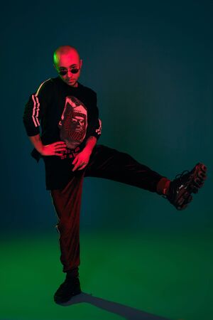 Studio shot of a young tattoed bald man posing against a colorful background. 90s style.