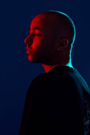 Studio shot of a young tattoed bald man posing against a blue background. 90s style.