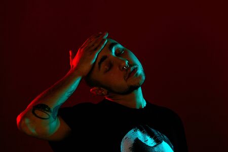Studio shot of a young tattoed bald man posing against a red background. 90s style.の写真素材
