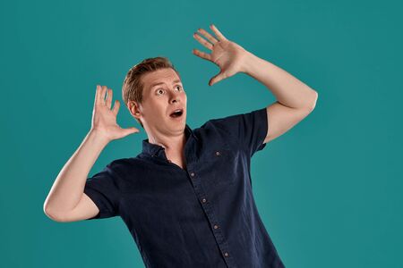 Close-up portrait of a ginger guy in navy t-shirt posing on blue background. Sincere emotions.