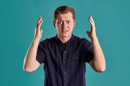 Close-up portrait of a ginger guy in navy t-shirt posing on blue background. Sincere emotions.